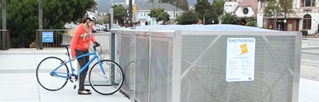A bicyclist pushes her bicycle into a metal bike locker.